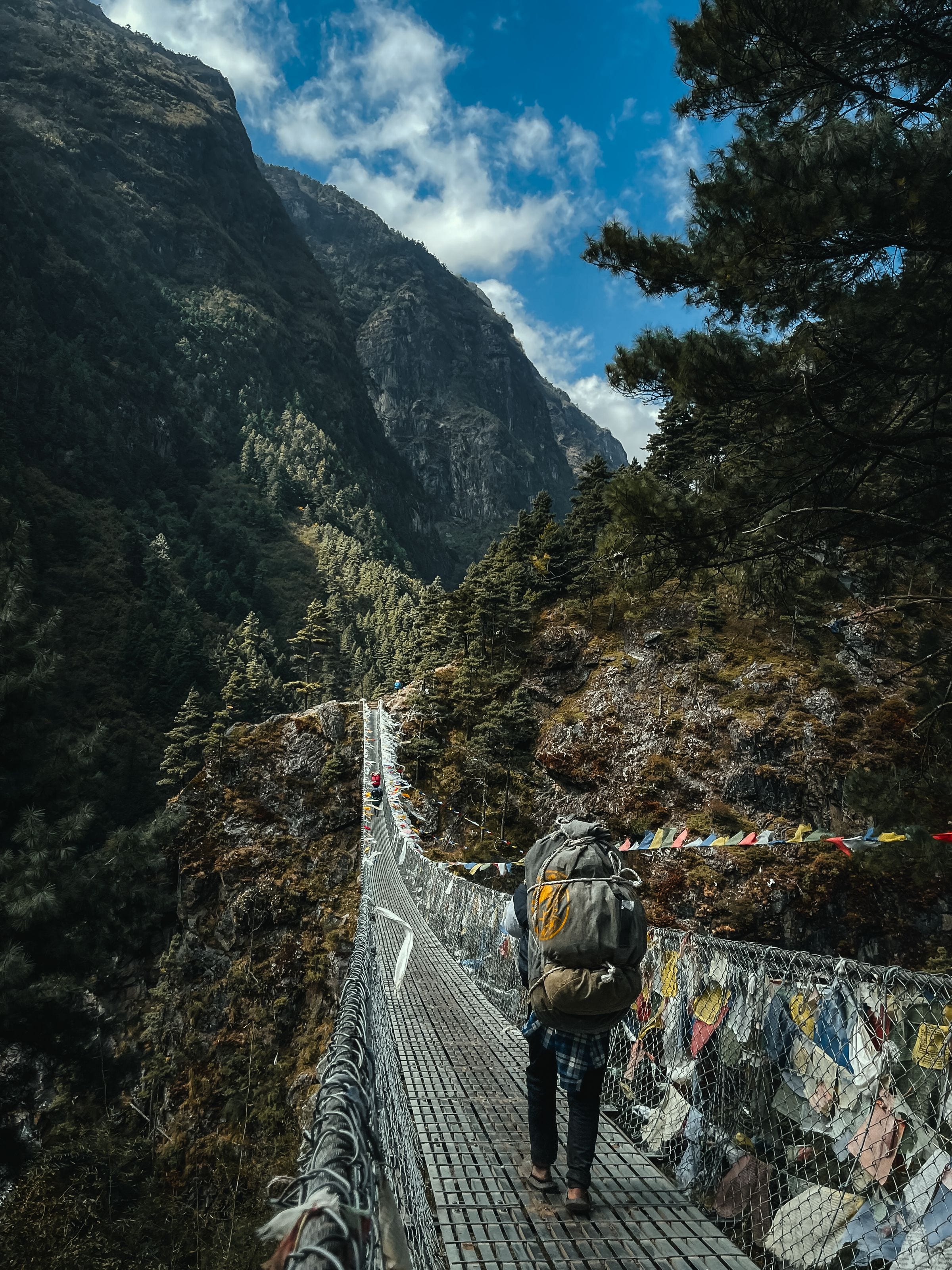 A trekker crossing a long suspension bridge over a forested gorge in the Khumbu
