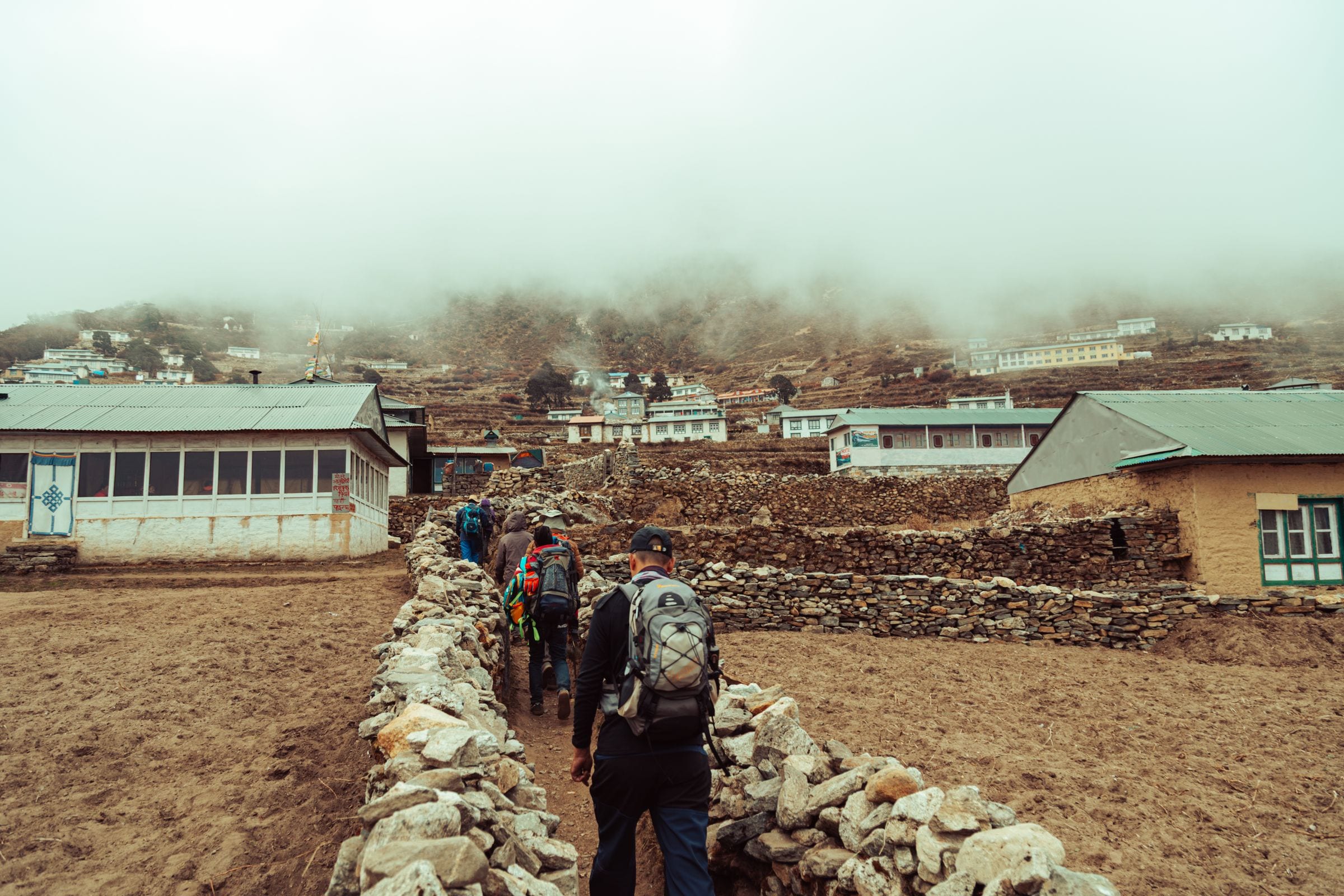 Trekkers on a stone path through a misty Himalayan village