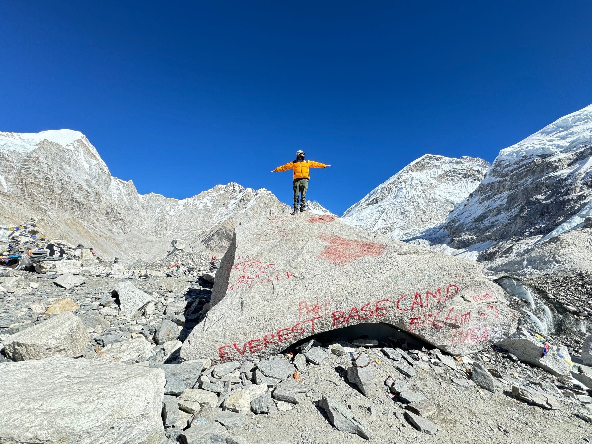 A trekker standing on the painted marker rock at Everest Base Camp