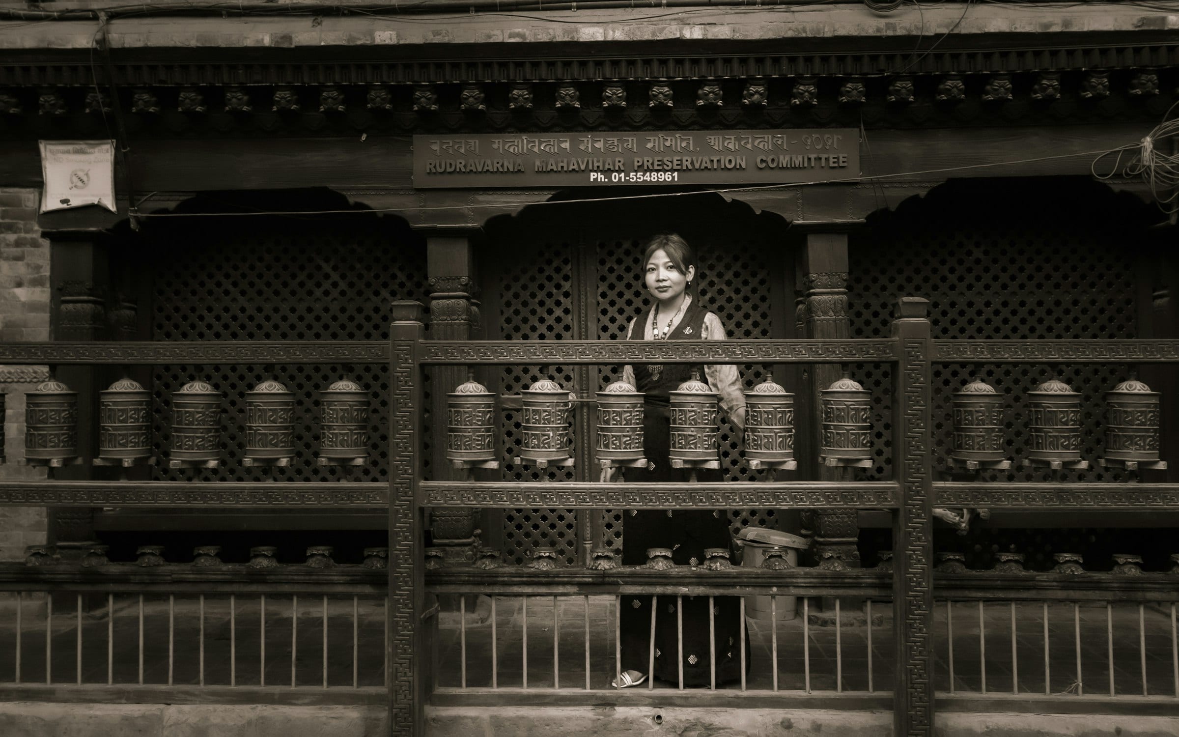A woman turning prayer wheels in a carved timber shelter