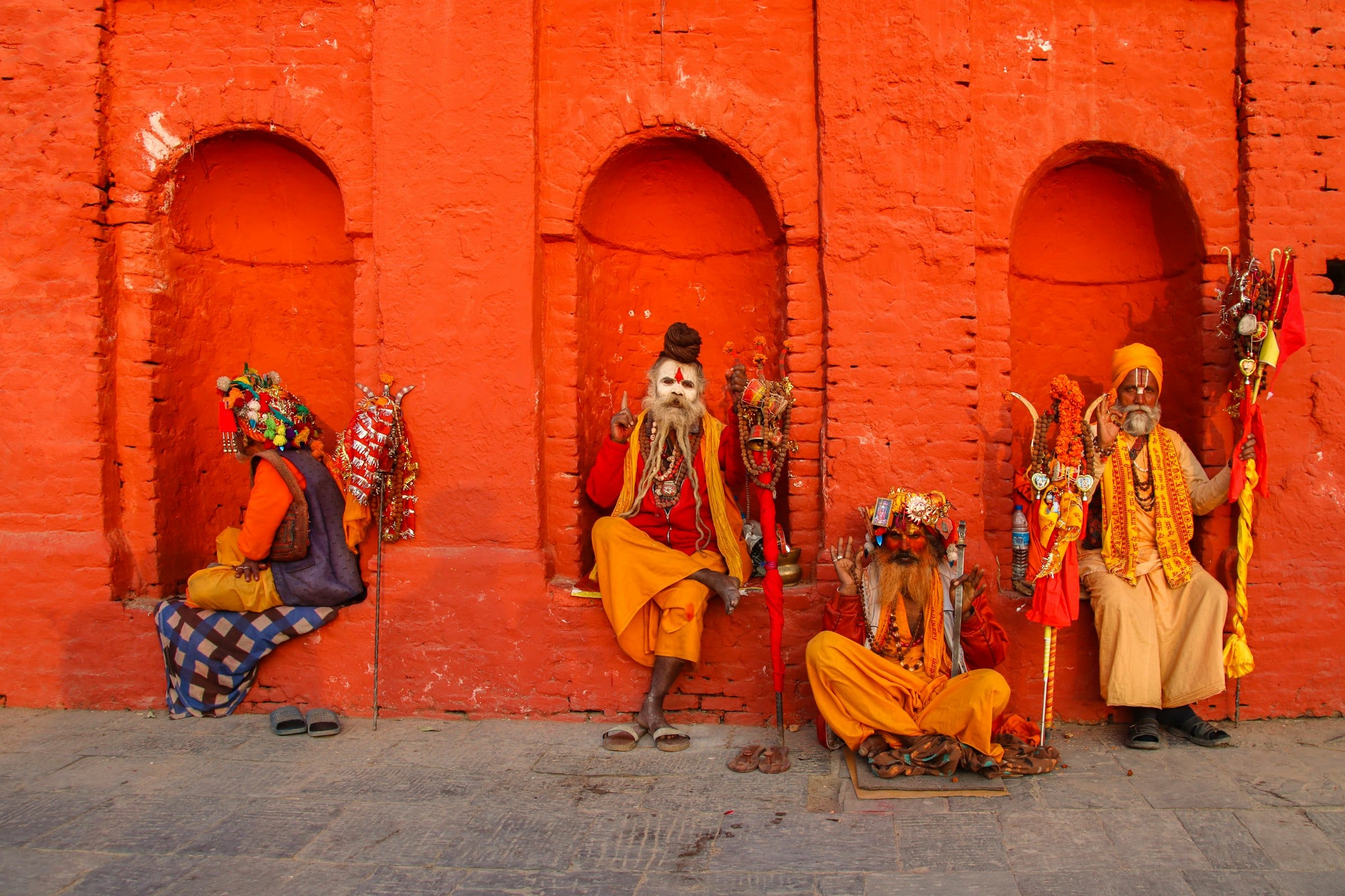 Sadhus in ochre robes seated against an orange temple wall