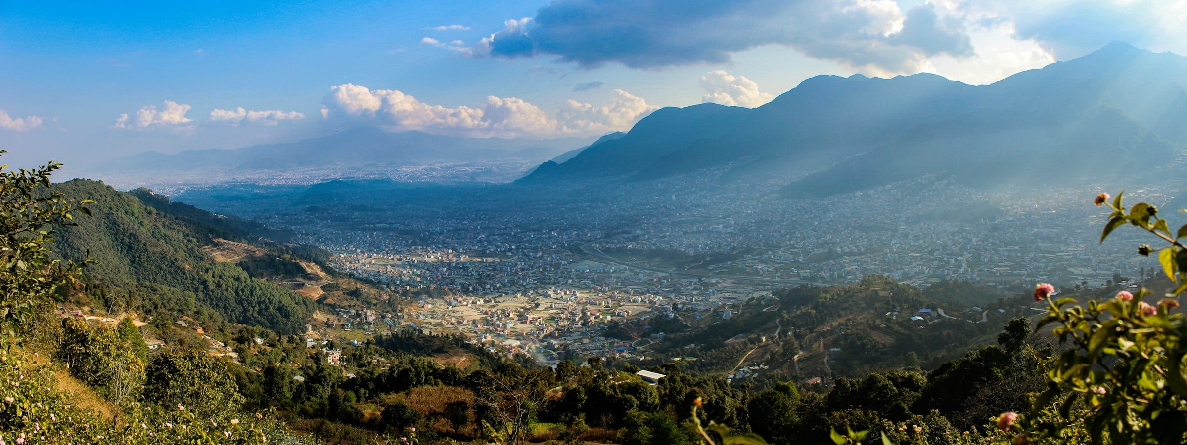 A valley town among green hills below the distant Himalaya