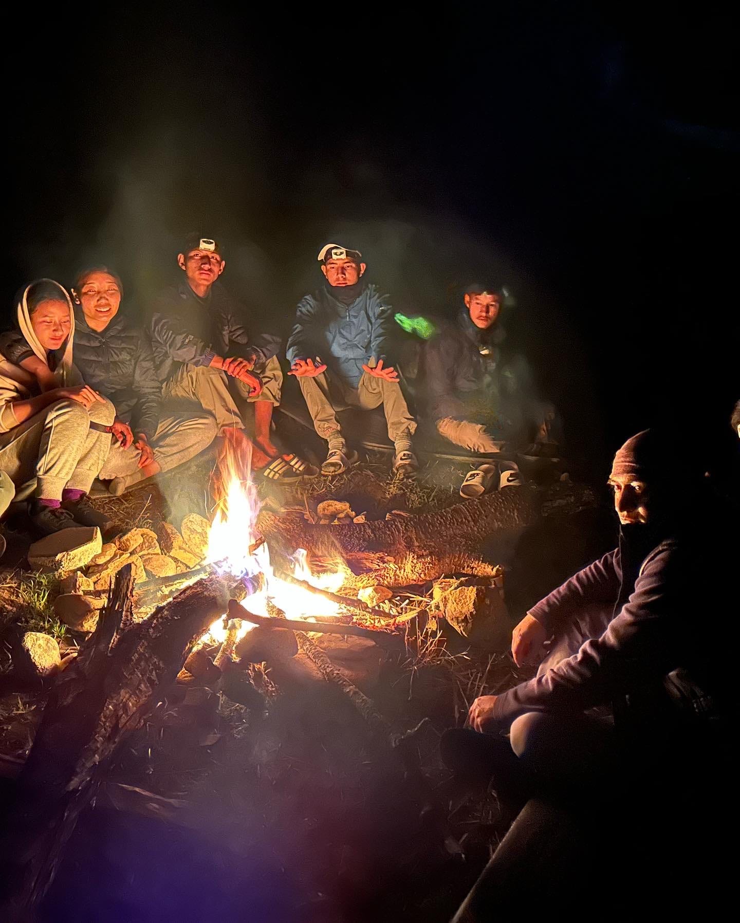 Students sitting around a campfire at night at camp