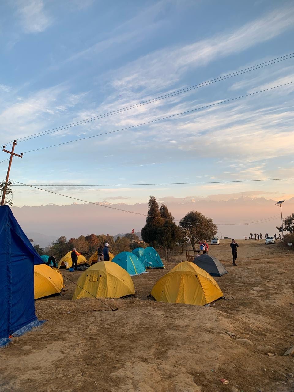 Yellow and blue tents on an open campsite at Dhulikhel, with a faint line of snow peaks on the horizon