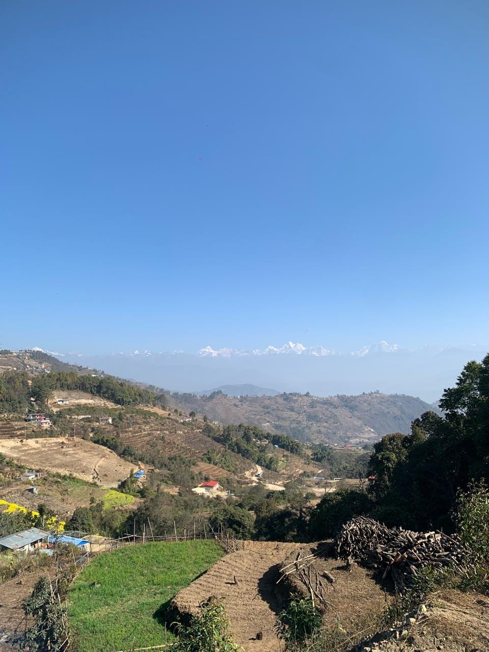 Terraced hillsides and scattered houses below Nagarkot, with snow peaks on the far horizon