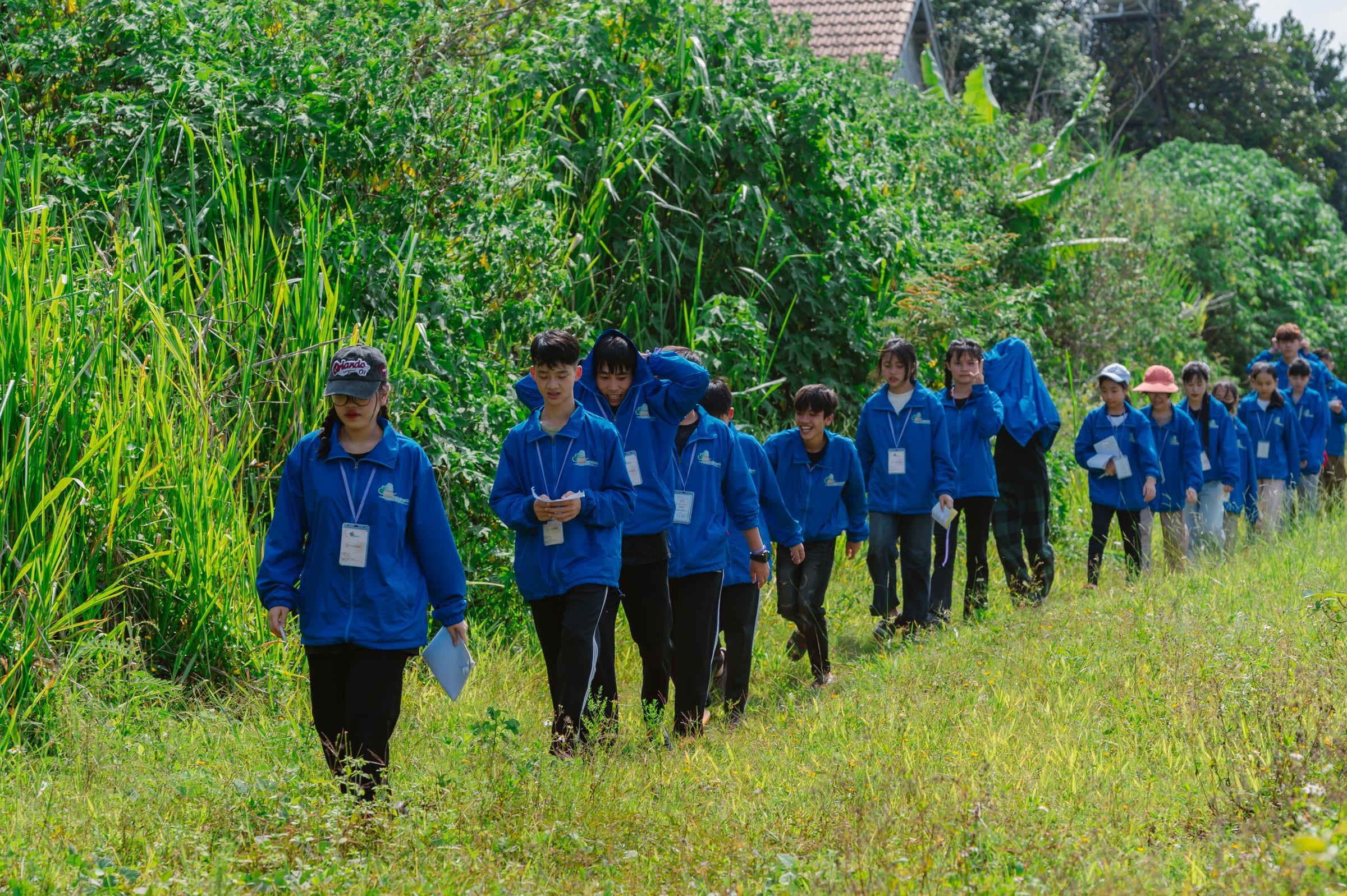 A school group in matching blue jackets walking single file along a grassy path