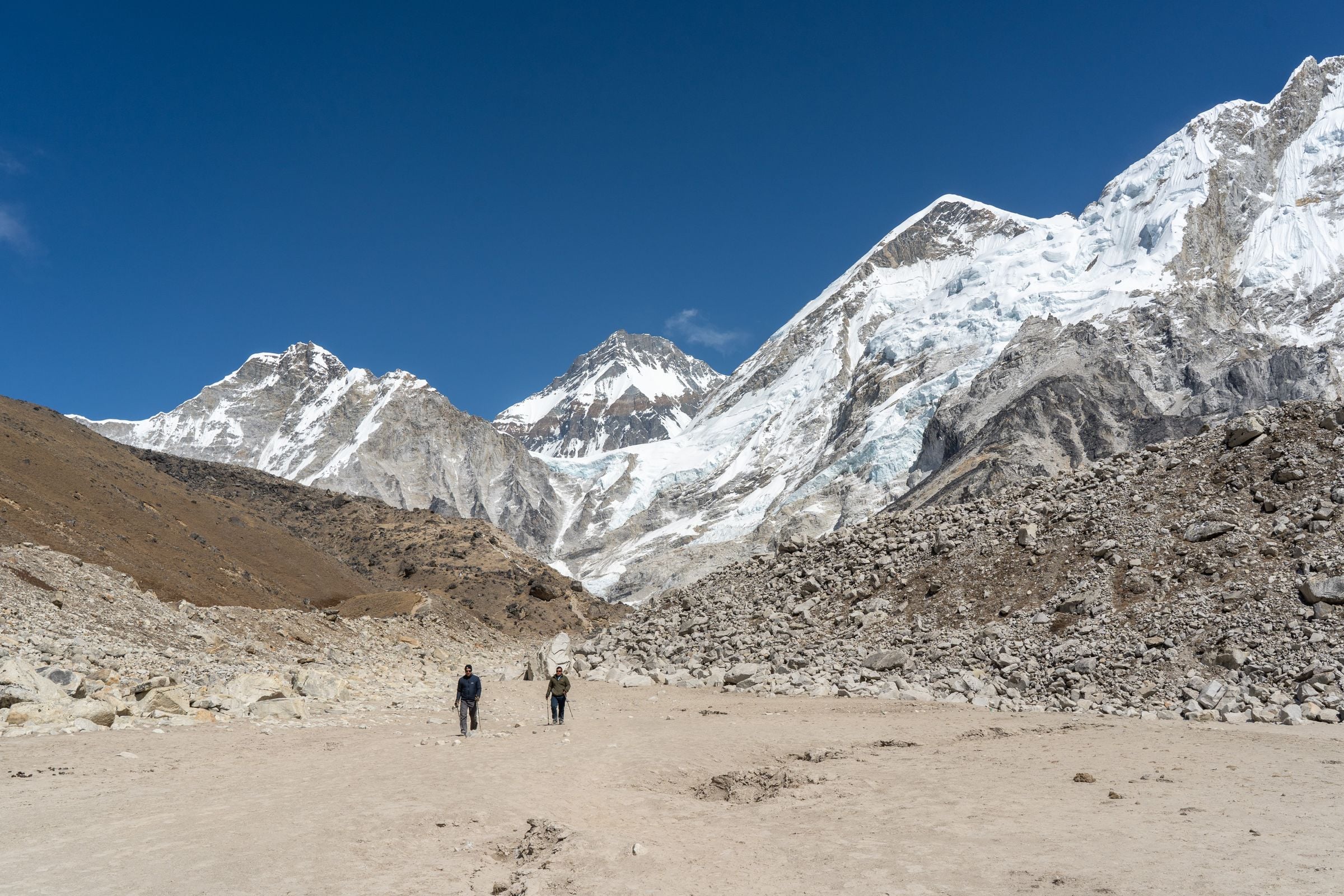 Two trekkers walking a broad glacial valley below the snow faces of Lhotse and Nuptse