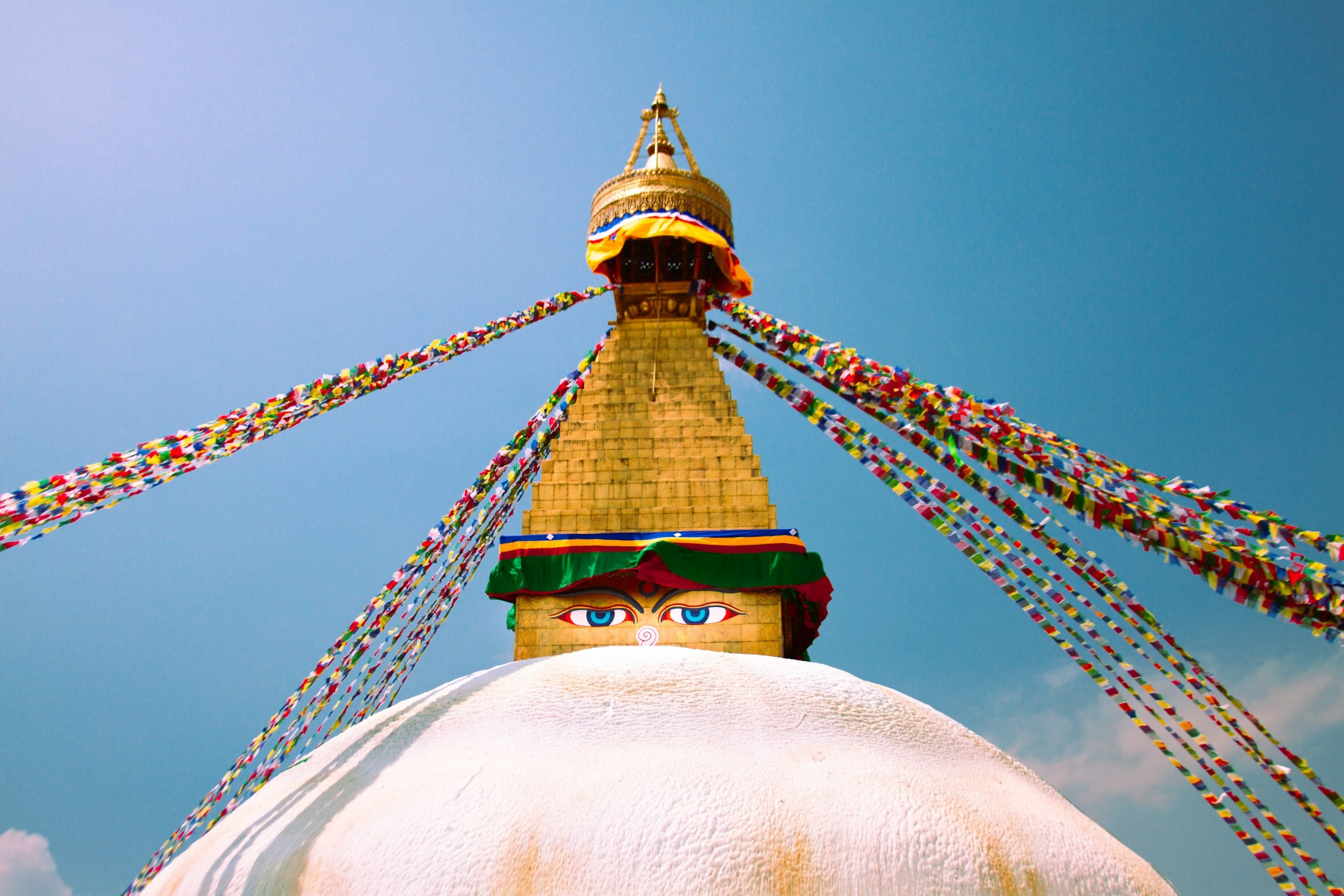 Boudhanath stupa under lines of prayer flags against a bright blue sky