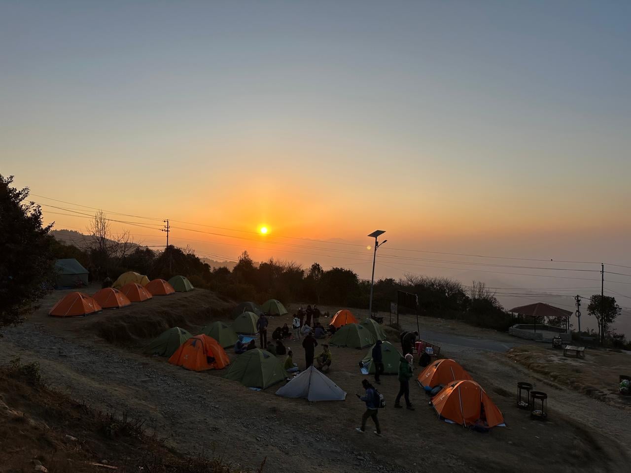 Orange and green tents pitched on a hilltop campsite at Nagarkot as the sun rises over the valley haze